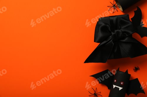 Preview: Paper bat, gift and spiders on orange background, space for text