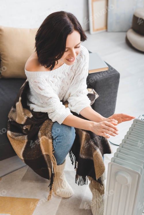 Preview: beautiful happy young woman with blanket in cold room with heater