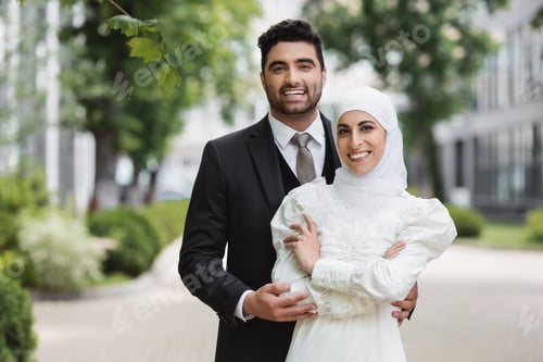 Preview: happy groom hugging muslim bride in hijab with wedding ring