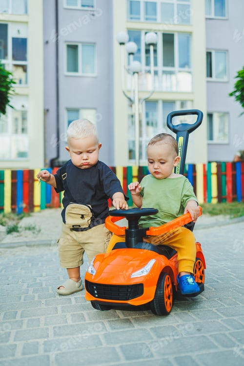 Preview: A one-year-old boy pushes a big toy car while playing outside. Children are playing in the street
