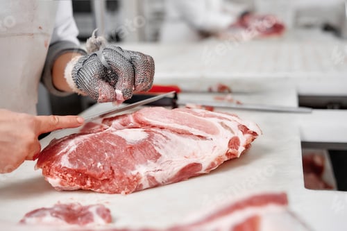 Preview: Close up of meat pieces and worker hands in gloves cutting