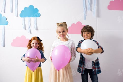 Preview: adorable happy kids holding balloons and smiling at camera at birthday party