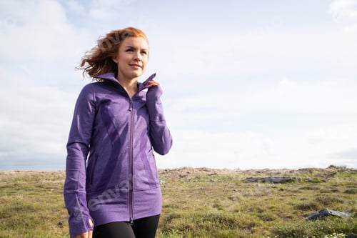 Preview: Redhead woman outside in countryside wearing purple workout jacket
