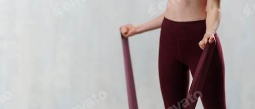 Preview: Close-up of sports woman in fashion sportswear exercising with elastic band stretch over greay