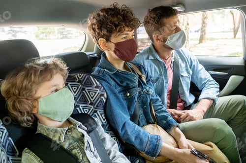 Preview: Row of contemporary young family of three in protective masks going by car