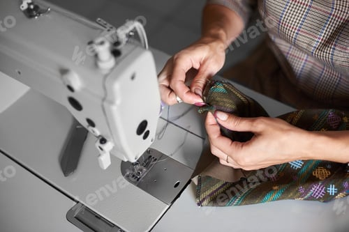 Preview: Seamstress working on modern electrical sewing machine making exclusive garments in fashion studio.