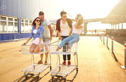 Preview: Group of happy young people having fun on shopping trolleys. Young people racing on shopping cart.