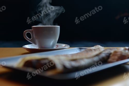 Preview: Selective focus shot of a white mug of hot coffee, and blurred crepes in a pub during snack time