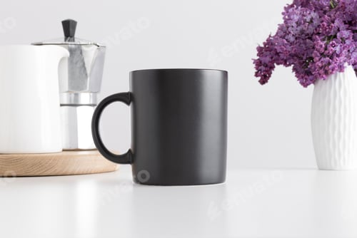 Preview: Black mug mockup with a moka pot and a bouquet of lilac in a vase on a white table.