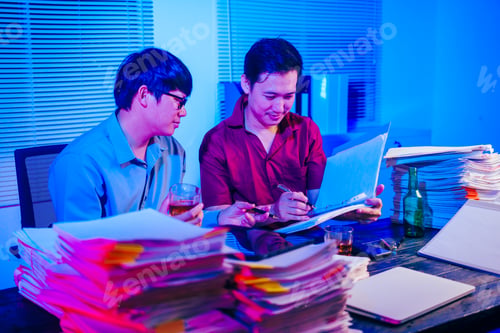 Preview: Two men are working late at office,drinking beer while checking documents.They are overwhelmed