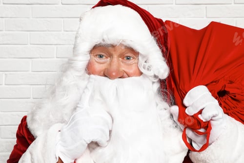Preview: Authentic Santa Claus with bag full of gifts against white brick wall