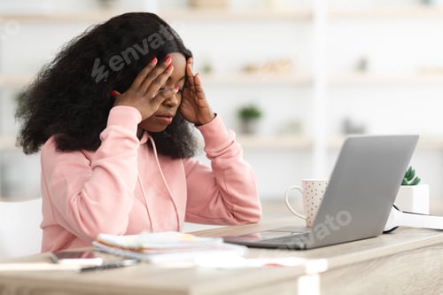 Preview: Stressed black woman sitting in front of laptop, touching head