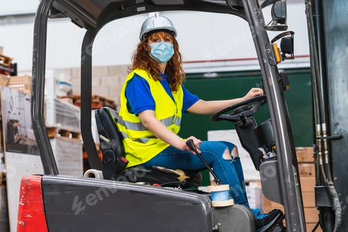 Preview: Industrial female worker wearing a medical mask using a loader in a warehouse