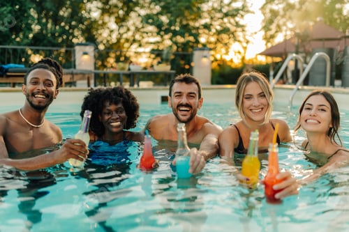 Preview: Group of friends enjoying drinks in swimming pool at sunset