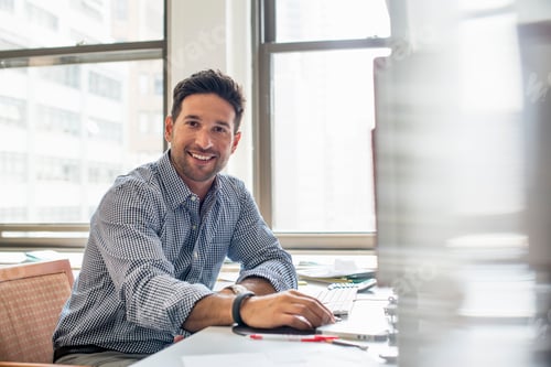Preview: Office life. A man sitting at a desk using a computer, looking at the camera.
