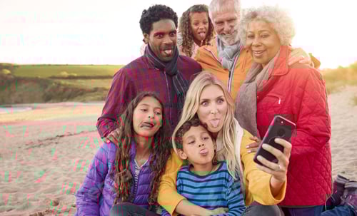 Preview: Multi-Generation Family Sitting By Fire On Winter Beach Vacation Taking Selfie