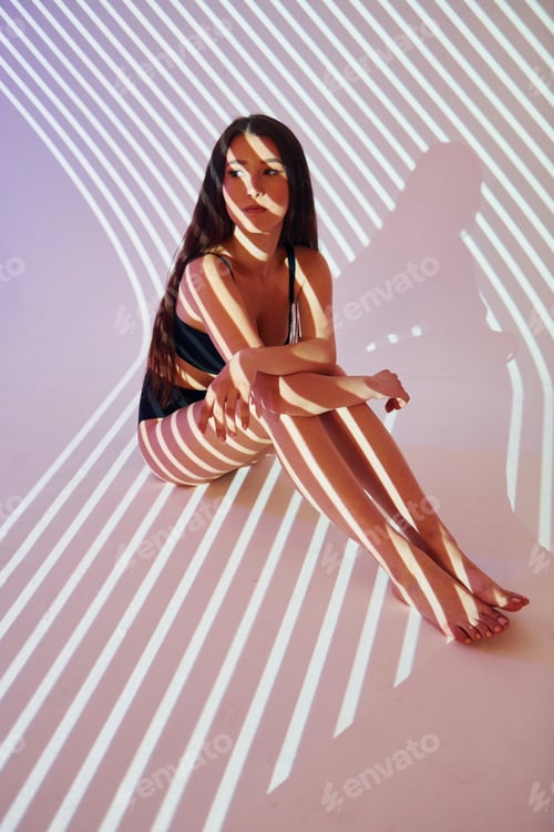 Preview: Sitting on the floor. Beautiful young woman is in projector neon lights in the studio