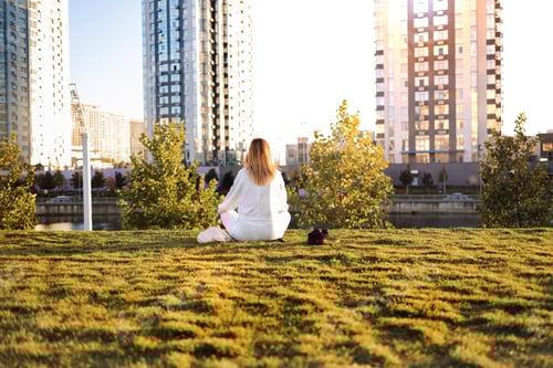Preview: Young woman meditating on the grass in the city park at sunset.