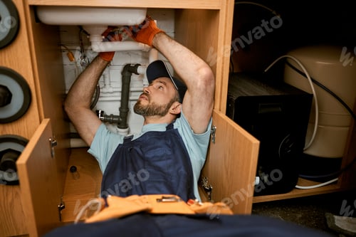 Preview: Male plumber repairing sink pipe in kitchen