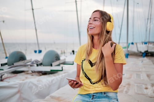 Preview: young woman with headphones seated on a boat at the beach