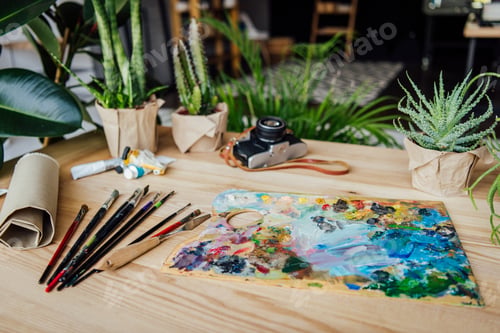 Preview: Wooden table full of potted green plants, art supplies and vintage camera