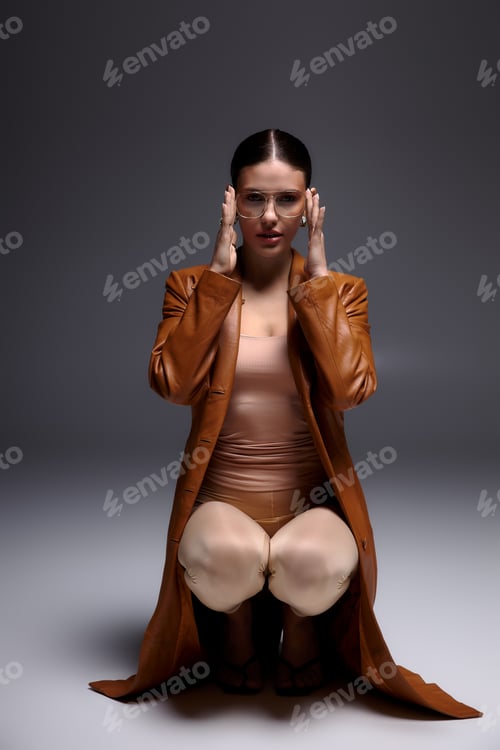 Preview: Stylish young woman poses in leather coat and glasses for a modern studio shoot