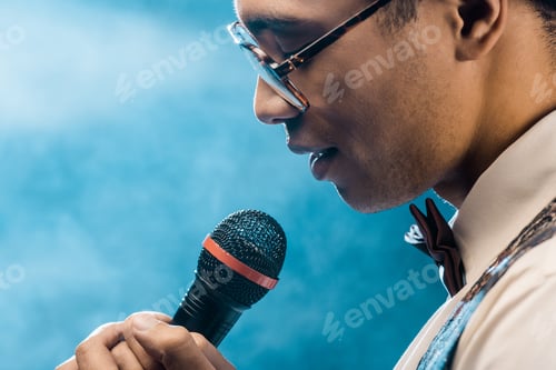 Preview: partial view of mixed race man singing in microphone on stage with smoke and dramatic lighting