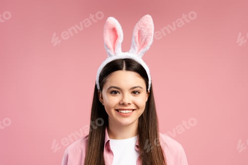 Preview: Happy young teen girl wearing bunny ears smiling on pink background