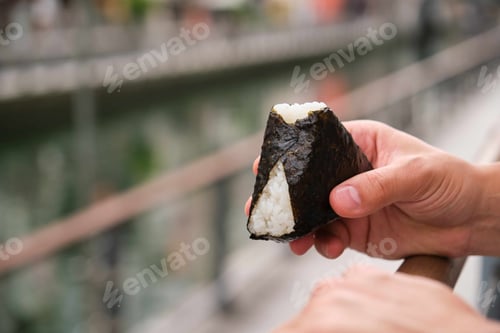 Preview: Unrecognizable person eating onigiri at street.