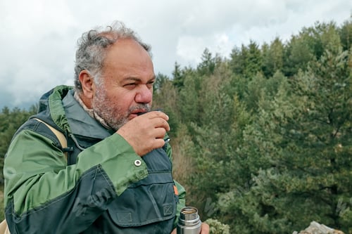Preview: Traveler man hiking in mountain forest, relaxing while drinking a cup of coffee from thermos