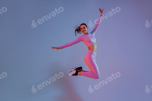 Preview: Smiling sporty woman in sportswear jumping on studio background. Sport and healthy lifestyle