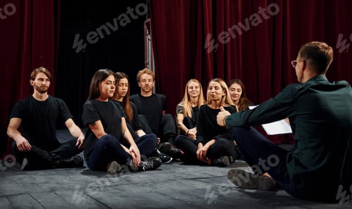 Preview: Sitting on the floor. Group of actors in dark colored clothes on rehearsal in the theater