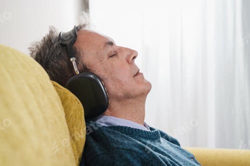 Preview: Senior man with headphones resting on couch, eyes closed in deep relaxation