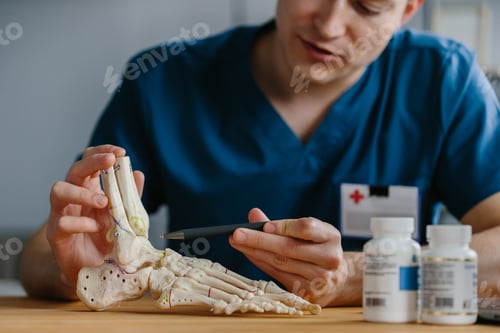 Preview: Young doctor using a foot skeleton model to explain a medical procedure in his office.