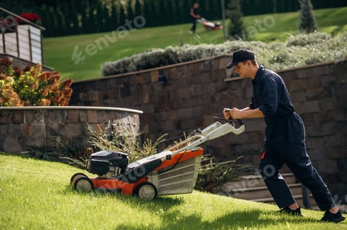 Preview: View from the side, cutting grass by lawn mover. Professional gardener is on the lawn