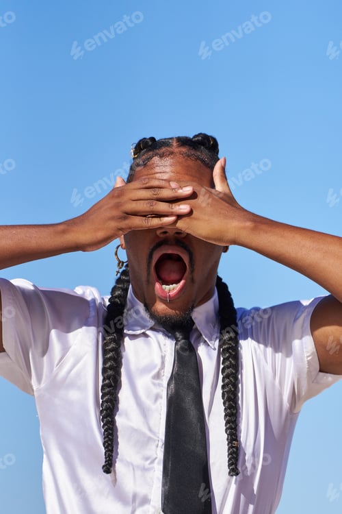 Preview: A man with braids and a black tie covers his eyes with his hands