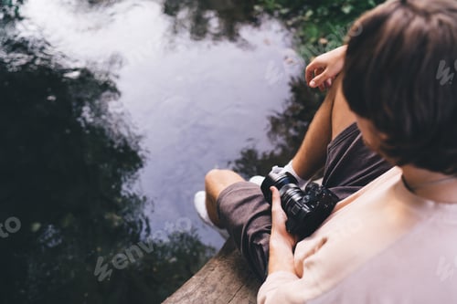 Preview: Anonymous man with photo camera sitting on tree trunk