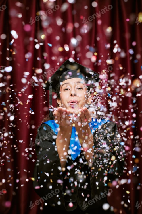 Preview: Young Adult Hispanic Woman Celebrating Graduation in Photo Booth Blowing Confetti