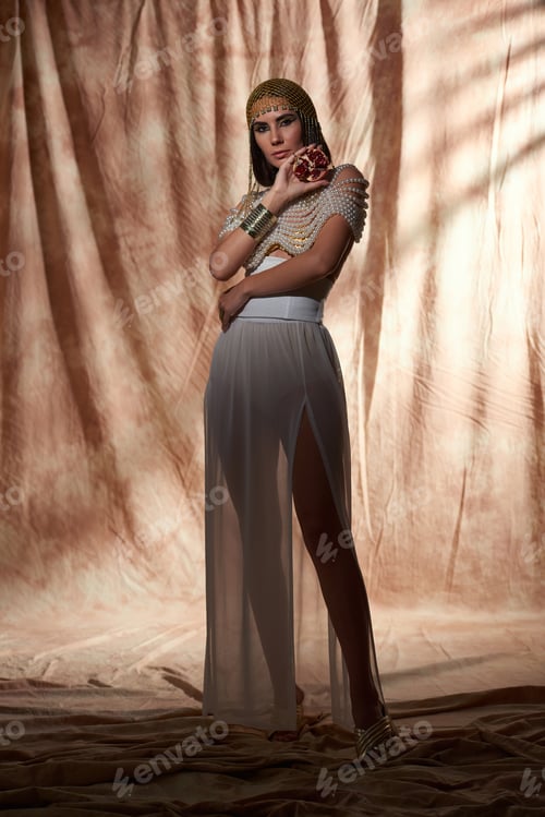 Preview: Full length of woman in egyptian attire and pearl top holding cut pomegranate on abstract background