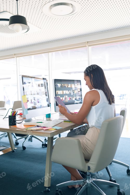 Preview: Side view of mixed race female graphic designer using digital tablet at desk in a modern office
