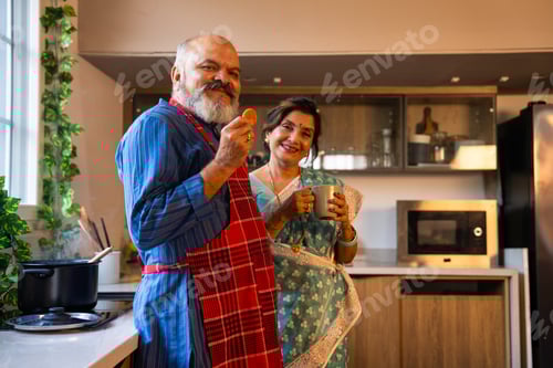 Preview: Charming Indian couple having tea in a modern kitchen, relaxing while waiting for their meal