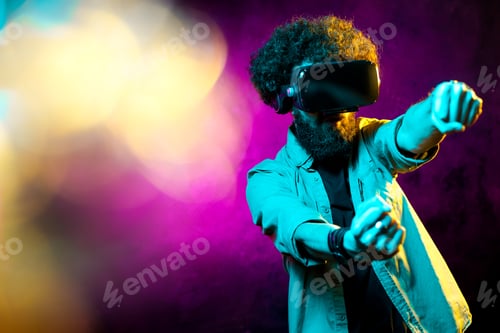 Preview: Young bearded hipster man wearing virtual reality goggles and touch another world in neon lights.