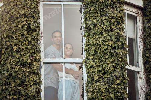 Preview: Happy young mixed race couple standing in their window. Loving couple bonding and spending time tog