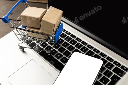 Preview: Composition of smartphone, shopping cart with boxes and laptop on wooden background