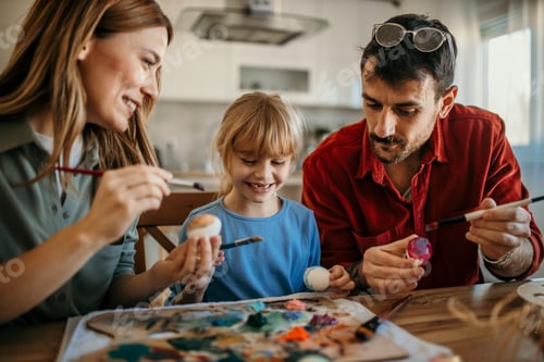 Preview: Parents and daughter painting colorful easter eggs together at home