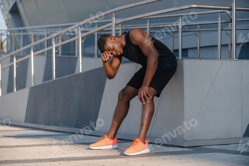 Preview: Full length of tired African man in sportswear resting after sports training outdoors