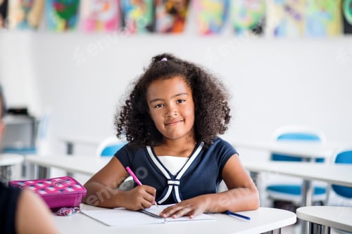 Preview: A small school girl sitting at the desk in classroom, writing.