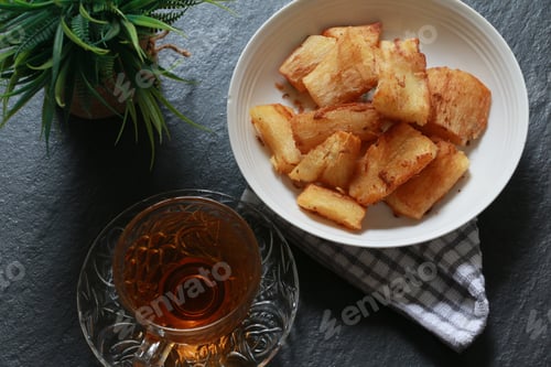 Preview: Fried cassava served with a cup of hot tea on dark slate background