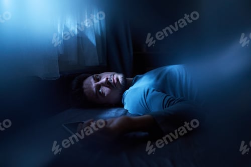 Preview: Young Man Lying Awake in Bed Holding Smartphone at Night