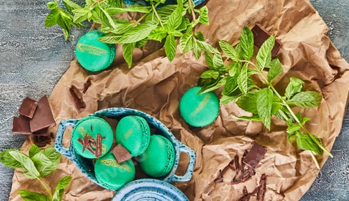 Preview: Green macarons topped with chocolate and mint leaves on a table